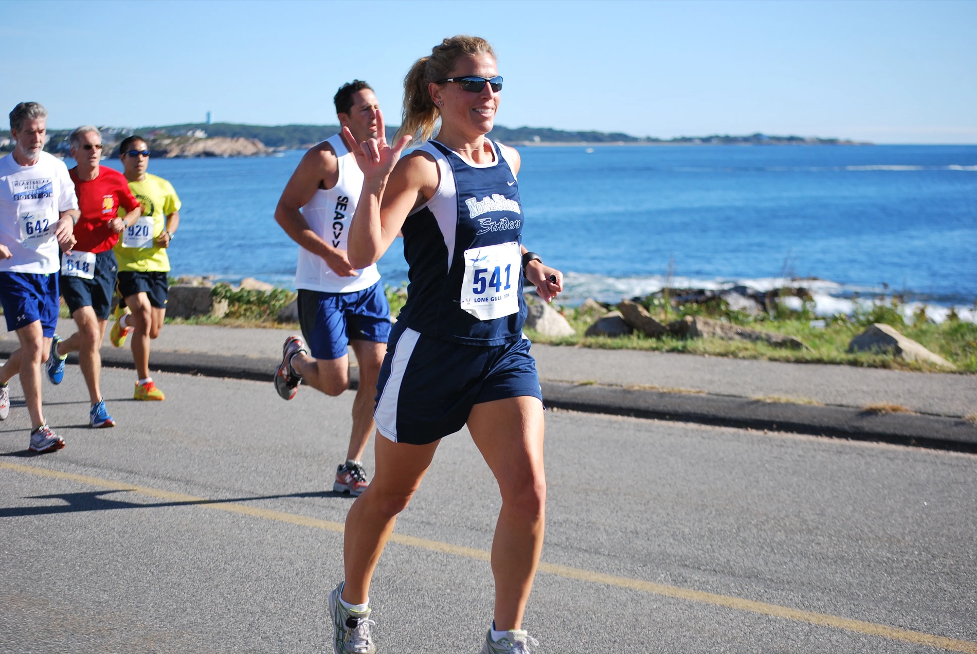 A Lone Gull 10K runner flashes the ASL sign for 'I love you' along the sunny Cape Ann coast